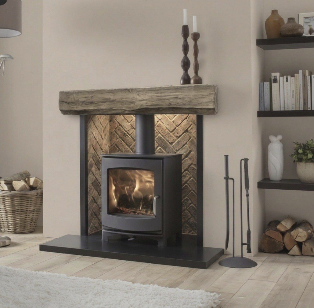 A wood burning stove in a herringbone brick chamber with an oak beam mantel